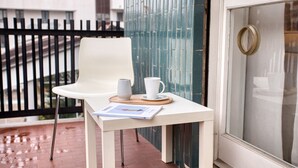 A white table with a chair, a white mug, and a magazine on a balcony with a glass door and a metal railing. - Easylife - Exclusive Comfort in Porta Romana (Milano)