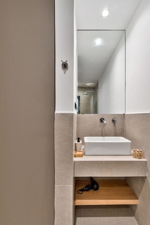 A modern bathroom with a white sink, a mirror, and a shower area.