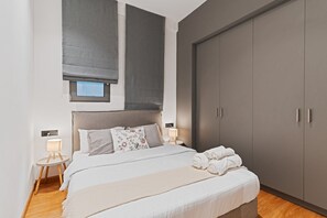 A modern bedroom with a large bed, bedside lamps, a wardrobe, and a window with blinds.
