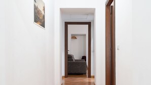 A hallway leading to a room with a gray sofa and a hanging coat rack.