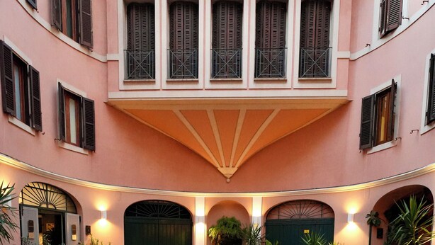 A courtyard with a central open space, potted plants, and a building with multiple windows and a green door.