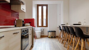 A kitchen with wooden cabinets, a red backsplash, a window, and a bar area with stools.