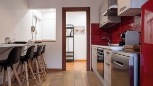 A modern kitchen with wooden flooring, a dining area with bar stools, and red-tiled backsplash.