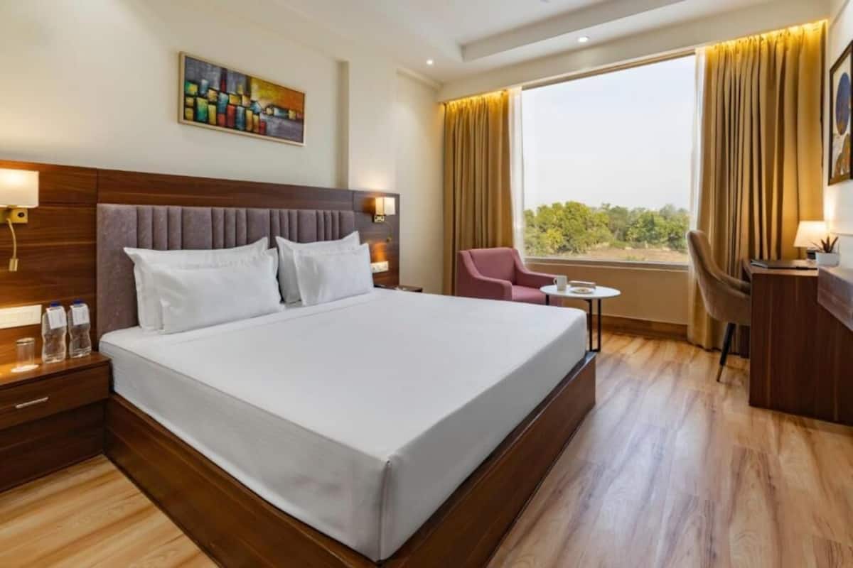 Une chambre d’hôtel avec un grand lit, un bureau, une chaise, une petite table et une fenêtre avec des rideaux.