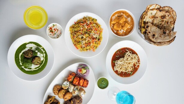 Une variété de plats, notamment du biryani, du paneer tikka et du pain naan, disposés sur une table blanche.