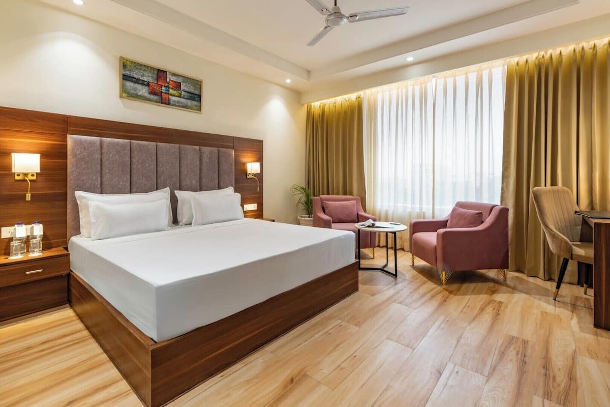 Une chambre d’hôtel avec un grand lit, un bureau, une chaise et un ventilateur de plafond.
