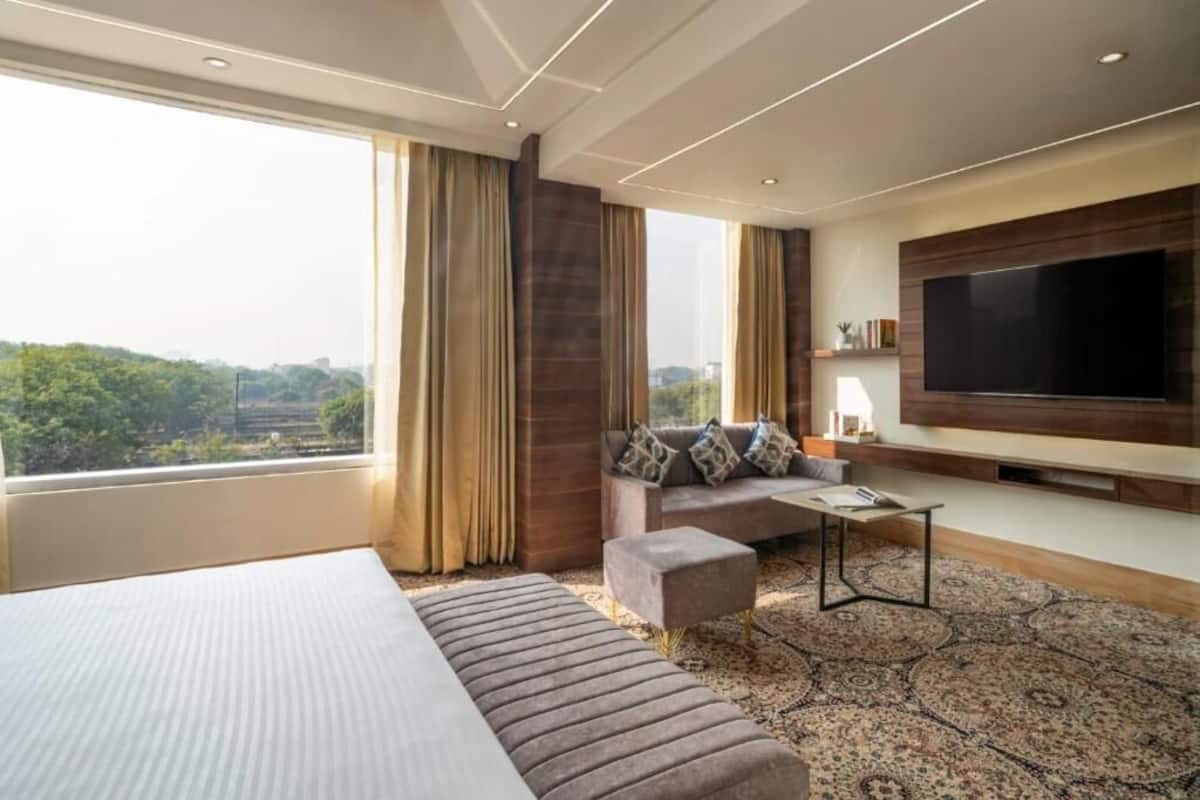 Une chambre d’hôtel moderne dotée d’un grand lit, d’un canapé, d’une télévision à écran plat et offrant une vue sur la verdure.