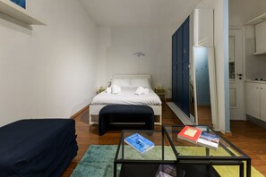 Ein Hotelzimmer mit Bett, kleinem Tisch mit Büchern, einer Couch und Blick auf die Küche.