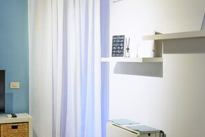 Une pièce avec un mur bleu, un rideau blanc, une étagère avec une pancarte et une petite table sur laquelle se trouve une télécommande.