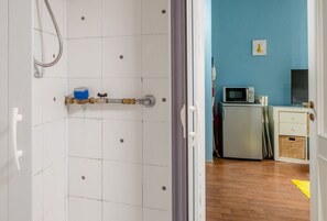 Une salle de bain avec des murs carrelés de blanc, une douche et un chauffe-eau apparent.