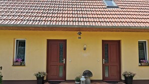 Ein Gebäude mit gelber Fassade, zwei braunen Türen und einem Ziegeldach.