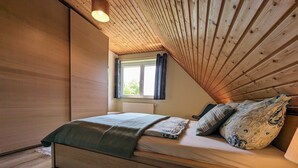 Ein gemütliches Schlafzimmer mit Holzbalkendecke, einem Bett mit gemusterten Betttextilien, einem Fenster mit Vorhängen und einer Heizung.