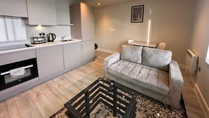 A modern kitchen with a built-in oven, a coffee maker, and a toaster. There is a grey sofa with a black and white patterned rug in front of it. - Cozy Studio in Bracknell with free Parking (Bracknell)