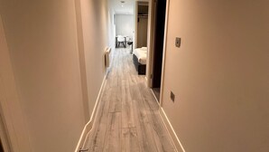 A narrow hallway with wooden flooring, leading to a room with a bed and a chair. - Cozy Studio in Bracknell with free Parking (Bracknell)