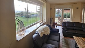 Amplia sala de estar con un gran ventanal, un sofá de cuero negro, una mesa de centro de madera y vistas al exterior.