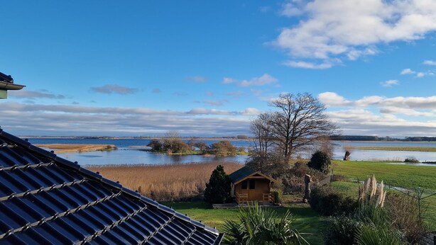 Vista de una propiedad junto al lago con una cabaña de madera pequeña, un campo cubierto de césped y una extensión de agua.