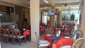 Un comedor con varias mesas y sillas, una pantalla de televisión y una zona de cocina al fondo.