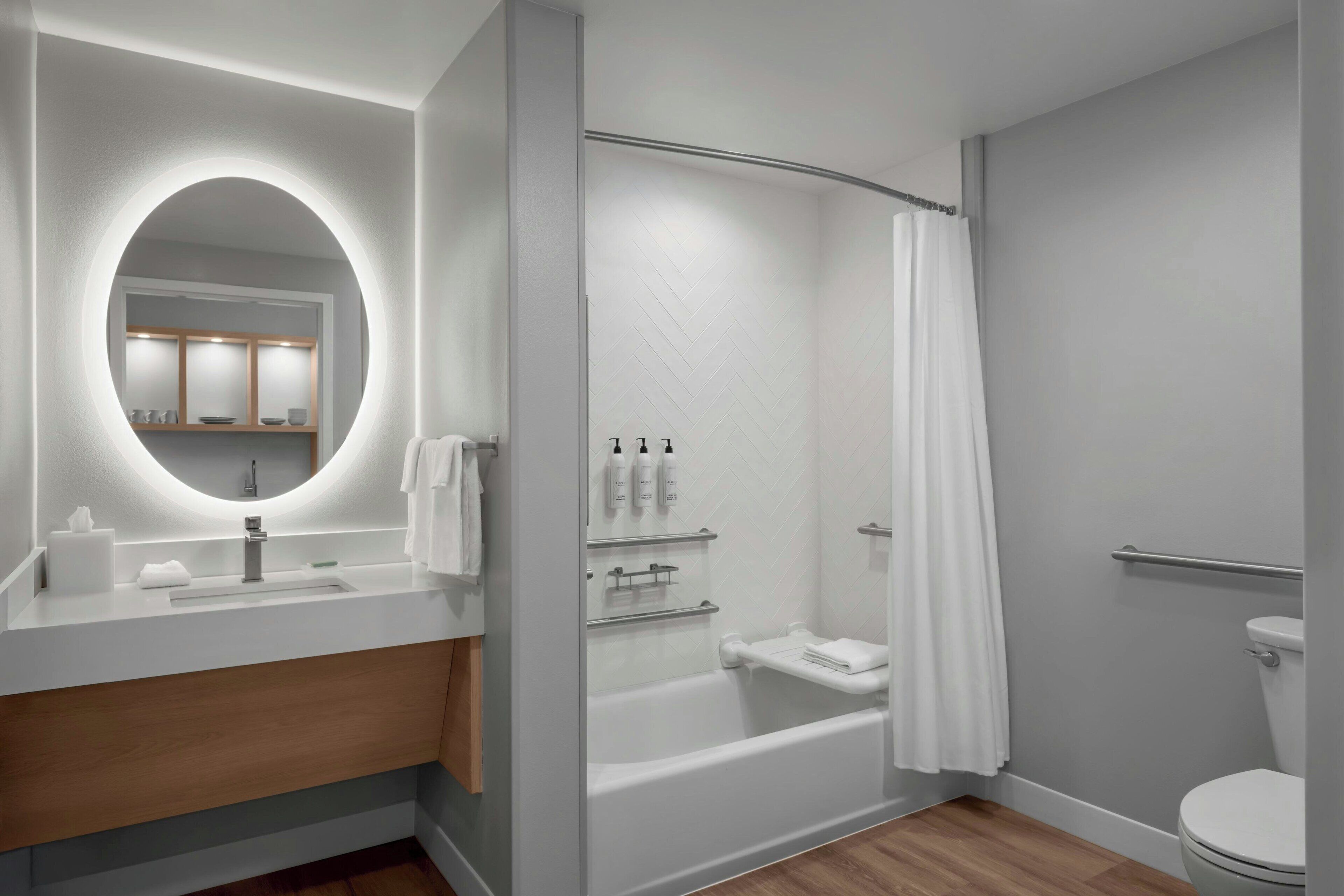 A modern bathroom with a round mirror, a bathtub, and a toilet.