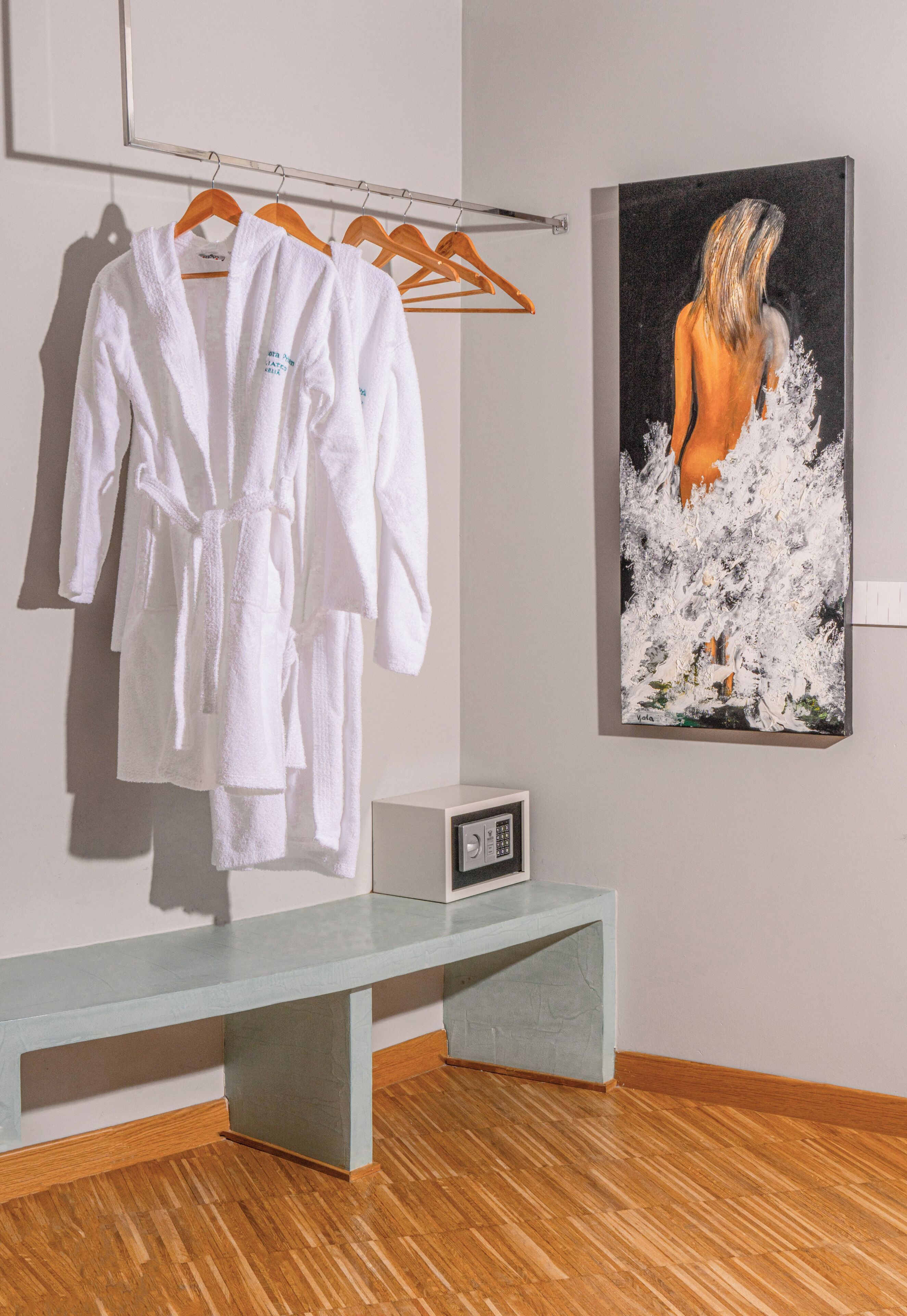 Um quarto com um banco, um cabideiro com roupões brancos e um quadro na parede.