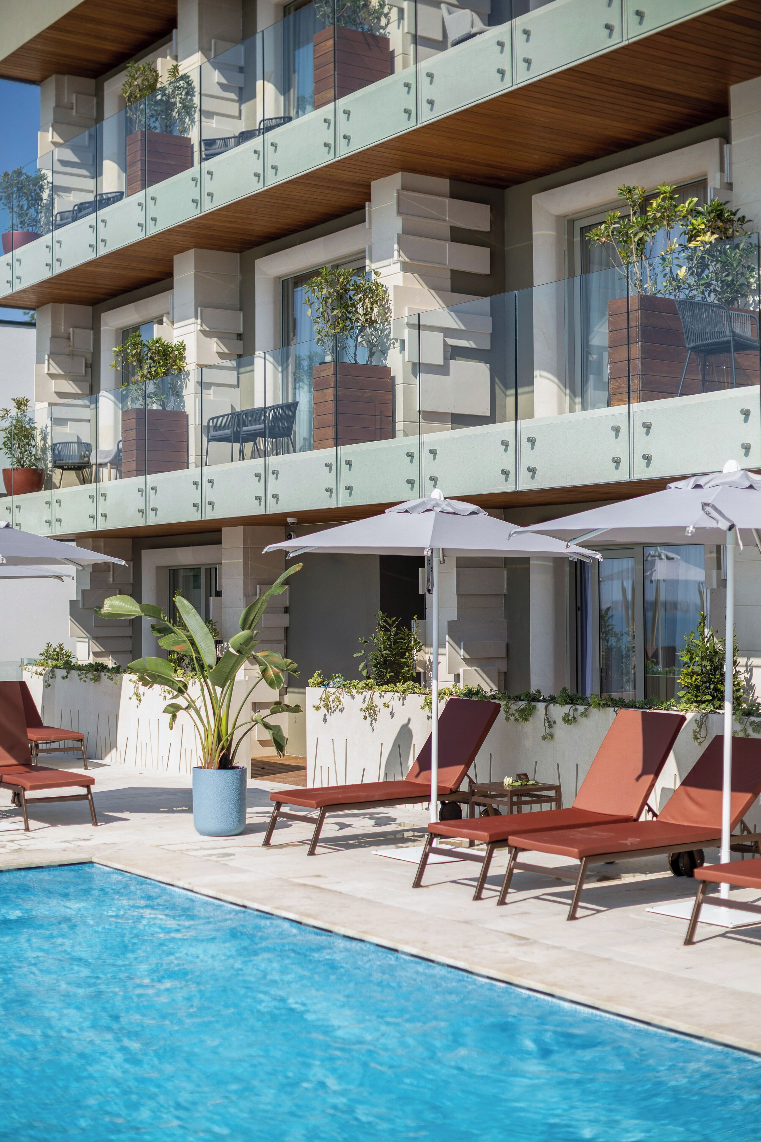Un hotel moderno con zona de piscina, sillones de descanso y plantas en macetas.