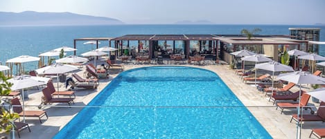 Una piscina al aire libre, sombrillas, sillones reclinables de piscina