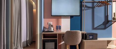 Une chambre d’hôtel comprenant un lit, un bureau avec un ordinateur, une chaise, un téléviseur, un porte-manteau et un mini-bar.
