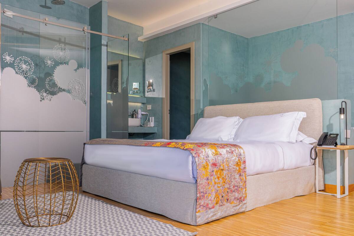 Quarto moderno com cama, mesa de cabeceira e cabine de chuveiro em vidro.