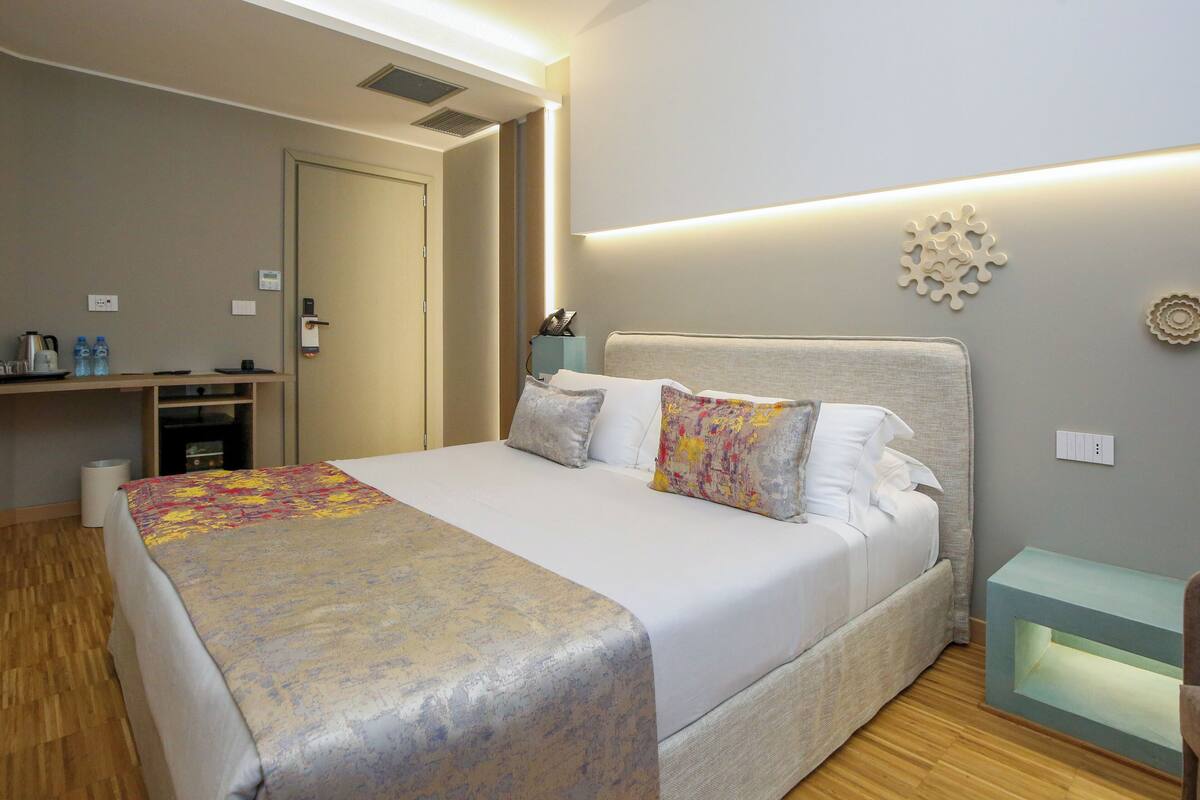 Quarto de hotel com cama, mesa de cabeceira e escrivaninha com cadeira.