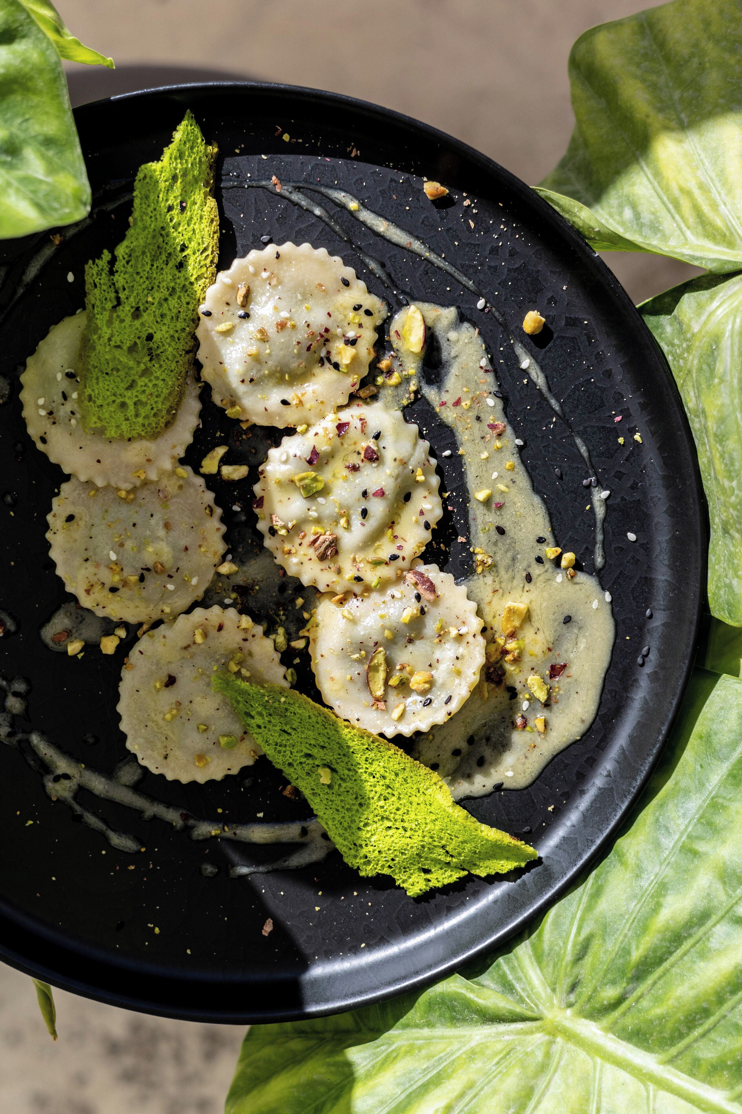 Une assiette noire contenant des raviolis, du pesto vert et des noix.