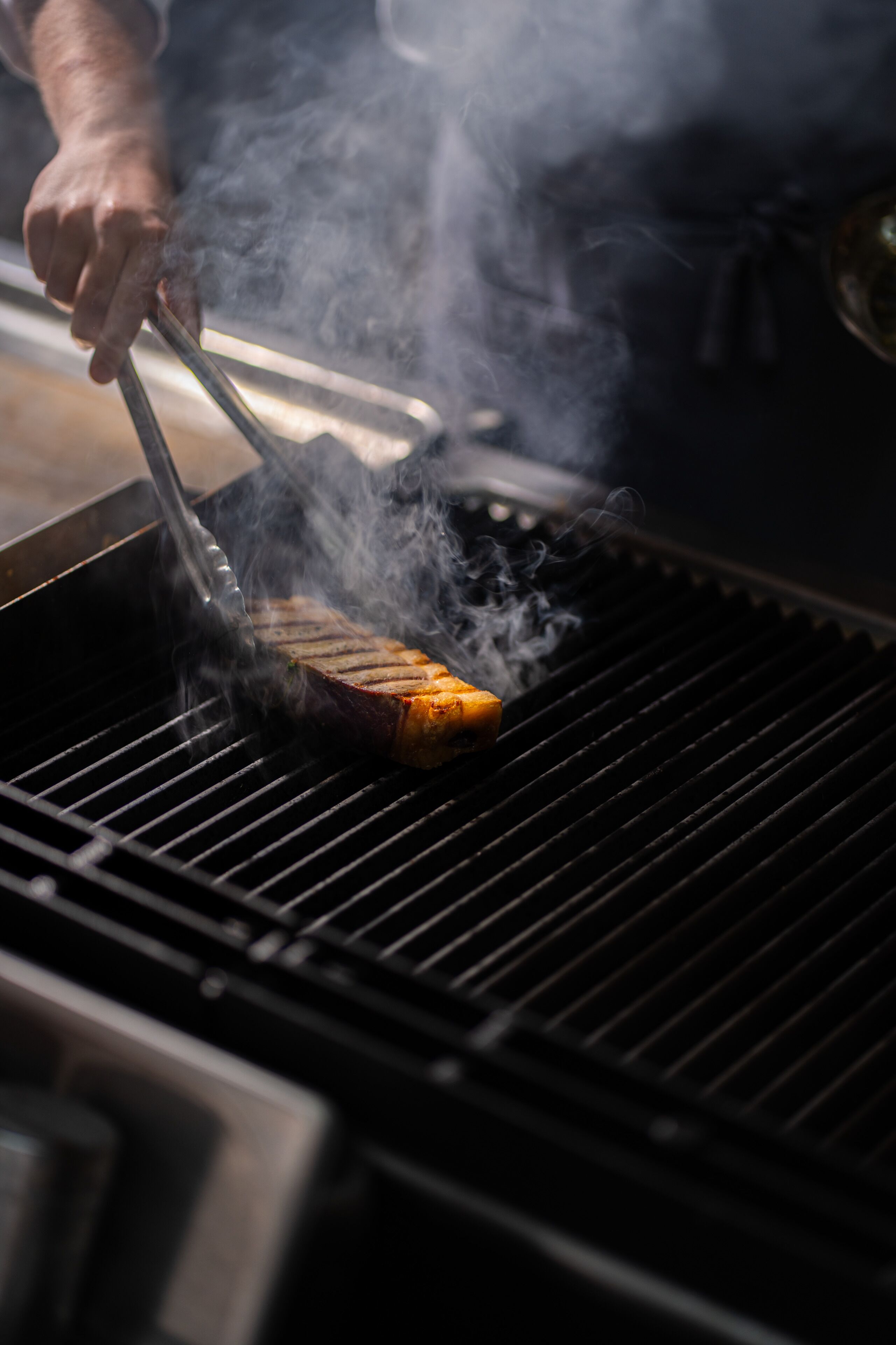 Una persona asando carne en una parrilla.