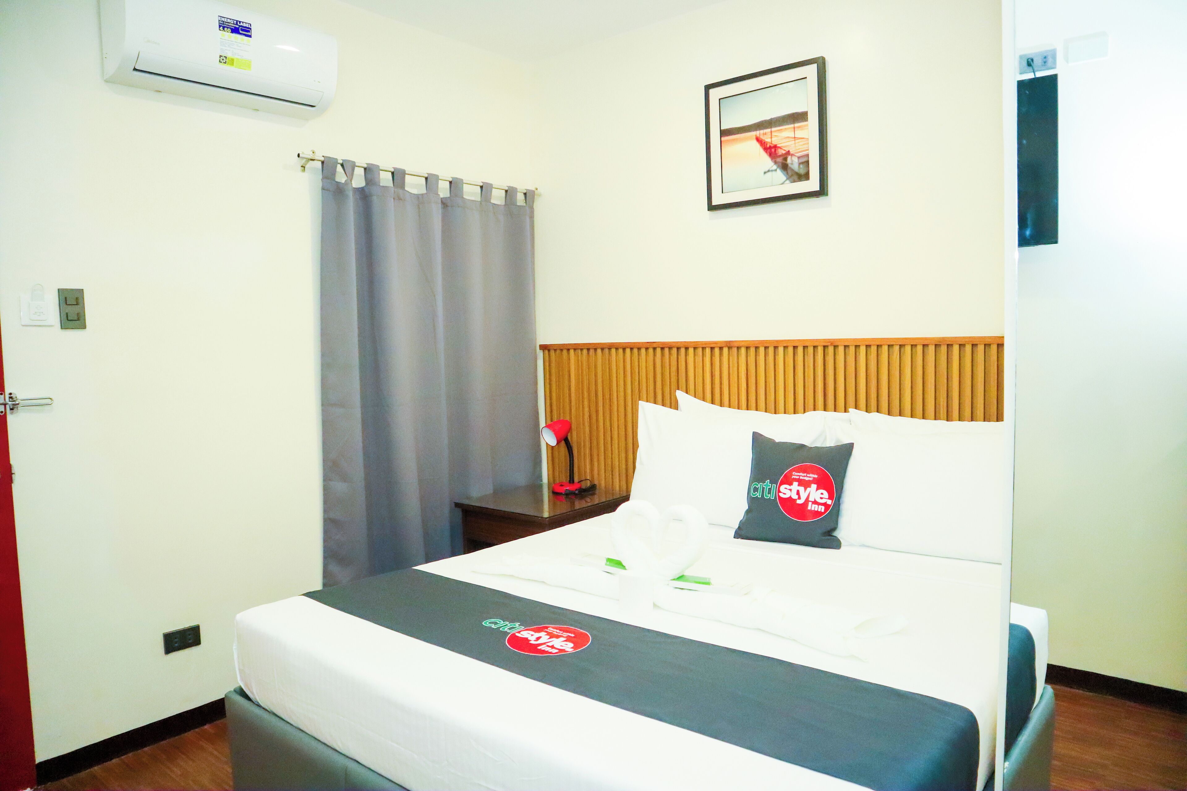 Une chambre d’hôtel comprenant un lit, une table de chevet, une lampe, une fenêtre avec des rideaux et un appareil de climatisation.