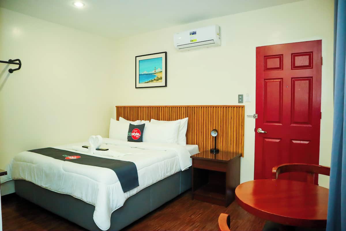 Quarto de hotel com cama, mesa de cabeceira, cadeira e uma porta vermelha.