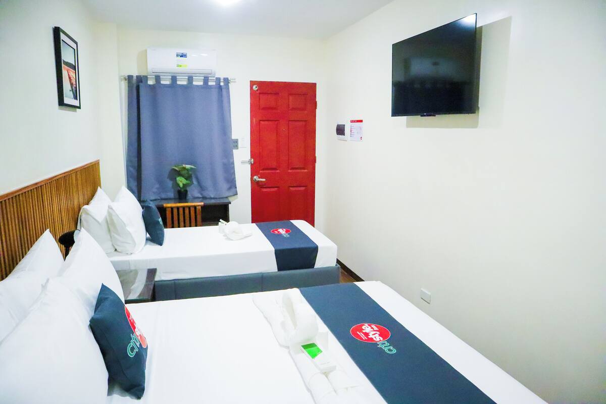 Quarto de hotel com duas camas, televisão, porta vermelha e cortina.