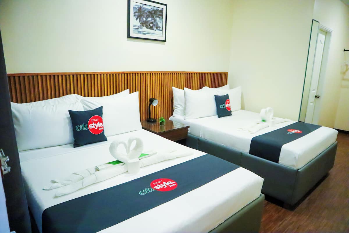 Quarto de hotel com duas camas, cada uma com colcha preta e branca estampada com um logotipo, arrumadas com toalhas brancas e um enfeite de cisne.