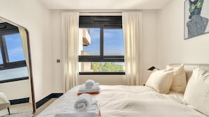 Habitación de hotel con cama, ventana con cortinas, un cuadro en la pared y vistas al exterior.