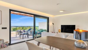 Una sala moderna con un amplio ventanal corredera que da a un espacio exterior, una mesa de comedor de madera y un televisor de pantalla plana.