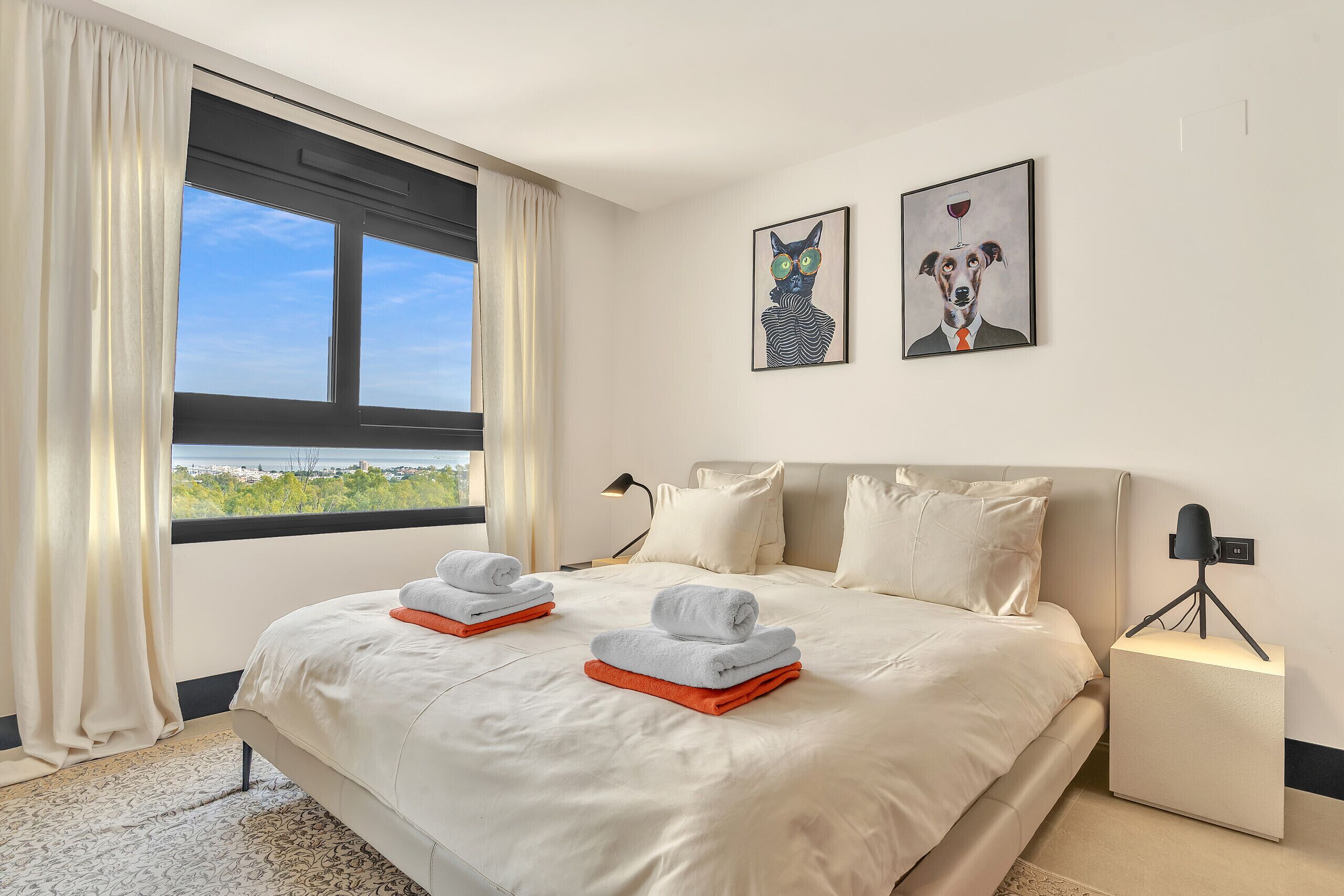 A bedroom with a large bed, two pillows, a nightstand with a lamp, and two wall art pieces.