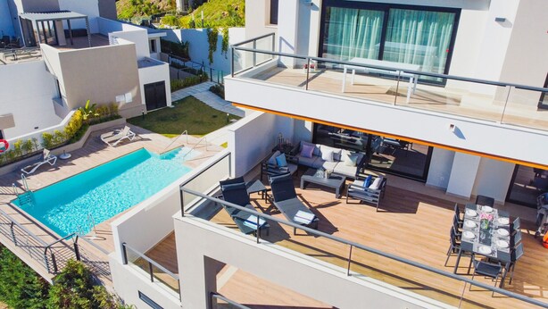 Un edificio moderno de dos pisos con piscina en la azotea, zona de estar al aire libre y comedor.