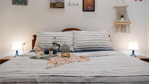 A neatly made bed with striped bedding, a macrame wall hanging, and a framed picture on the wall.