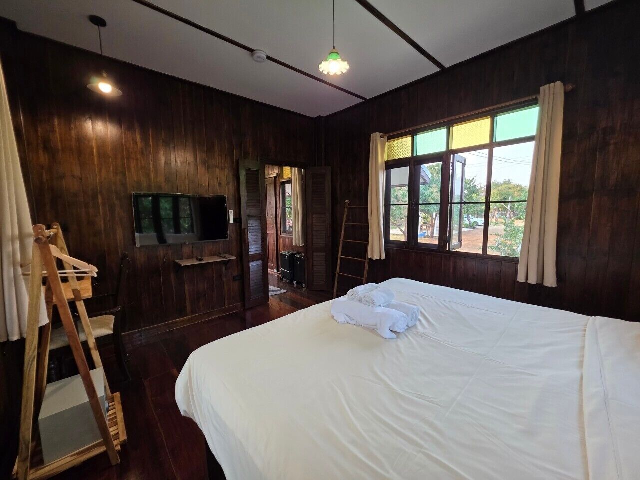 A room with a large bed, wooden walls, a television, and a window with curtains.