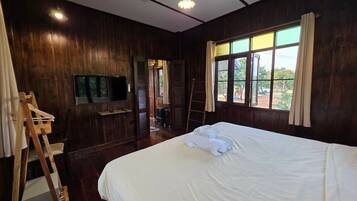 A room with a large bed, wooden walls, a television, and a window with curtains.