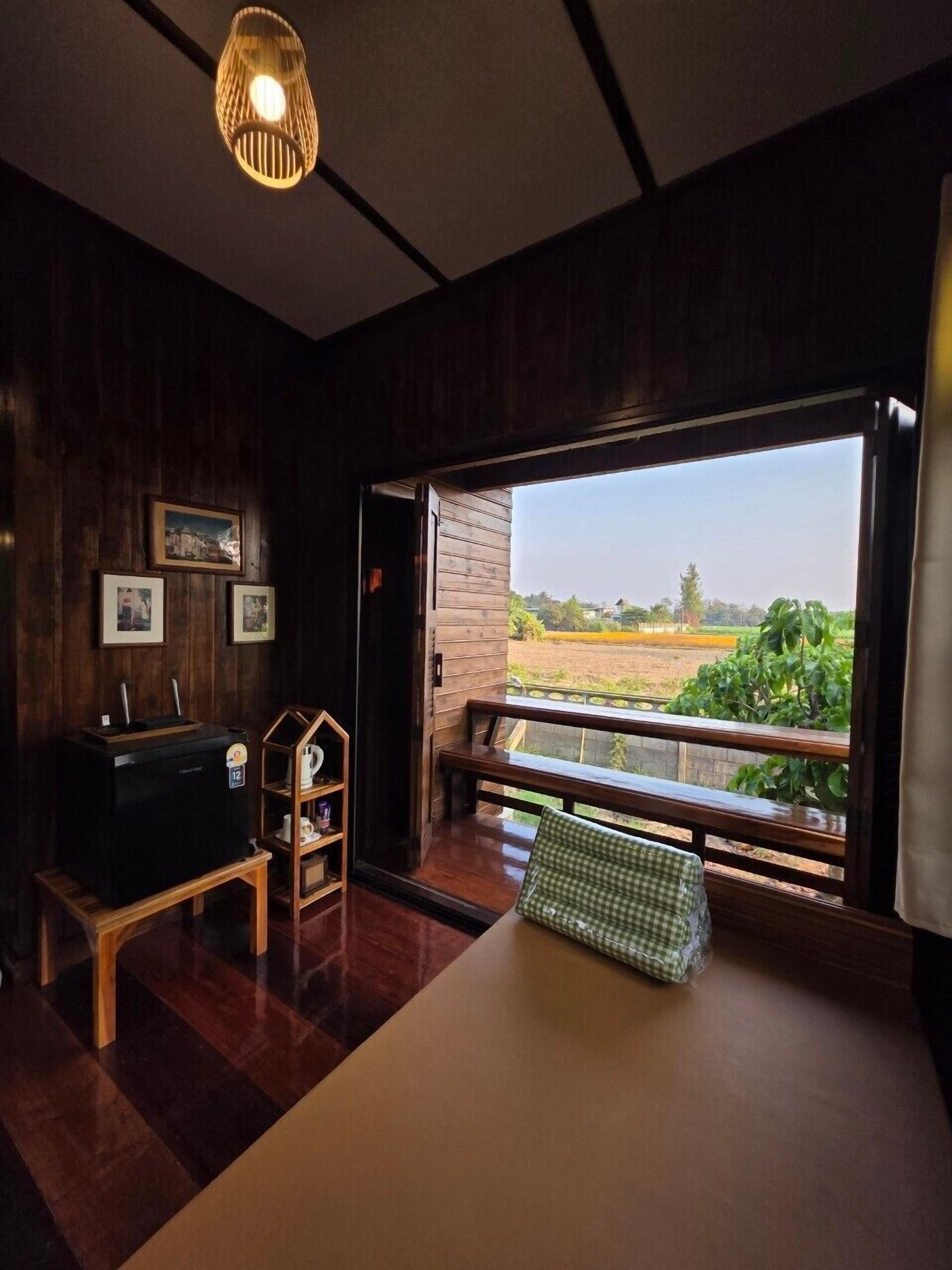 A room with a large window, wooden walls, a bed, a desk, and a hanging light fixture.