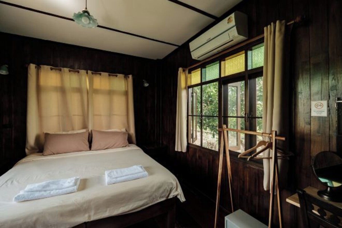 A bedroom with a bed, a window with curtains, an air conditioning unit, and a wooden hanger rack.
