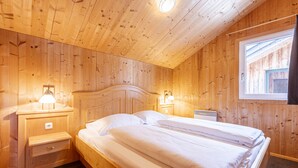 Un dormitorio con paneles de madera, una cama, mesitas de noche y un ventanal.