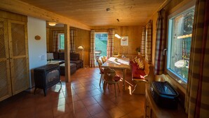 Ein gemütliches Blockhauss-Interieur mit Essbereich, Kamin und großem Fenster mit Vorhängen.