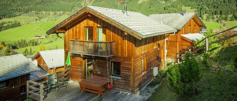 Une cabane en bois dotée d’un balcon, entourée d’un paysage verdoyant et luxuriant, avec des montagnes en toile de fond.