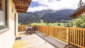 Eine Holzterrasse mit Tisch und Stühlen mit Blick auf eine gebirgige Landschaft.