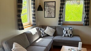 Ein modernes Wohnzimmer mit einem grauen Ecksofa, einem Holztisch und einem gerahmten Kunstwerk an der Wand.