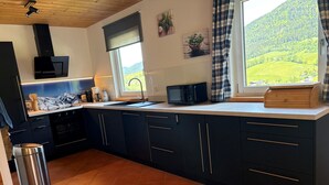 Eine moderne Küche mit dunklen Schränken, einem Edelstahl-Mülleimer und Blick auf eine grüne Landschaft durch ein Fenster.