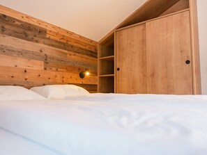 A bedroom with a wooden headboard, a bed with white bedding, and a wardrobe with two doors. - Superior Chalet # 61 with 3 BR and IR-Sauna (Annaberg)